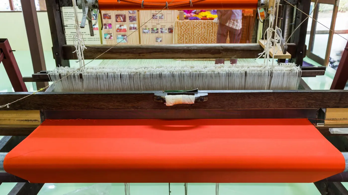 Thai silk being woven by hand on a traditional wooden loom